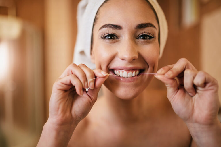 Young woman cleaning her teeth with a dental floss in the bathroom